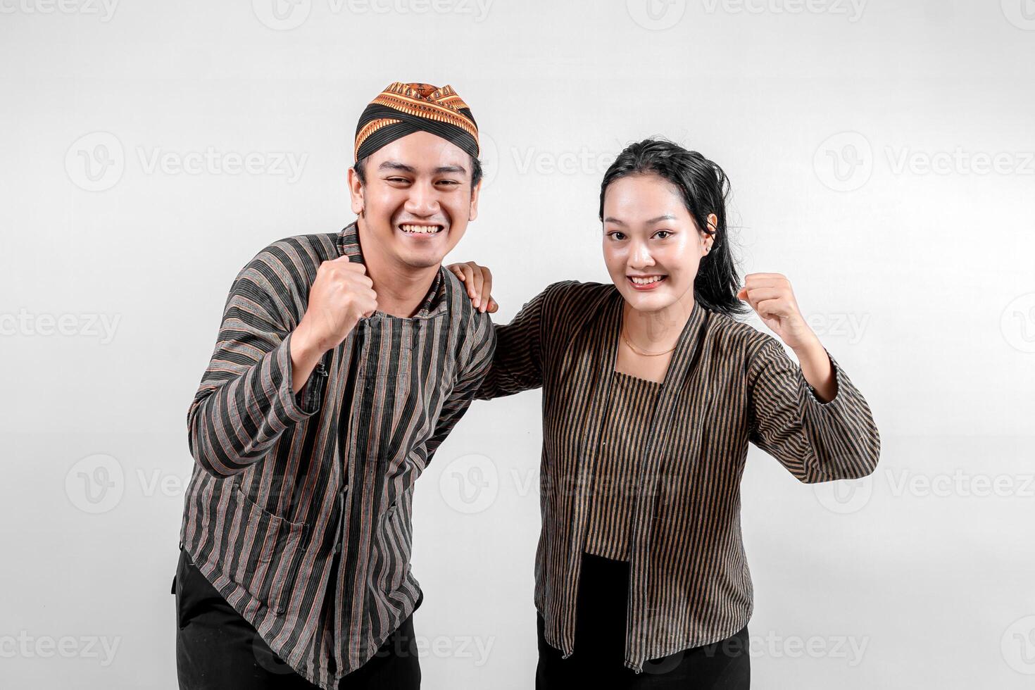 a Indonesian couple wearing traditional Javanese Lurik or Sorjan clothing, smiling with fists raised. Cultural striped outfit, symbolizing heritage and resilience. Isolated on white. photo
