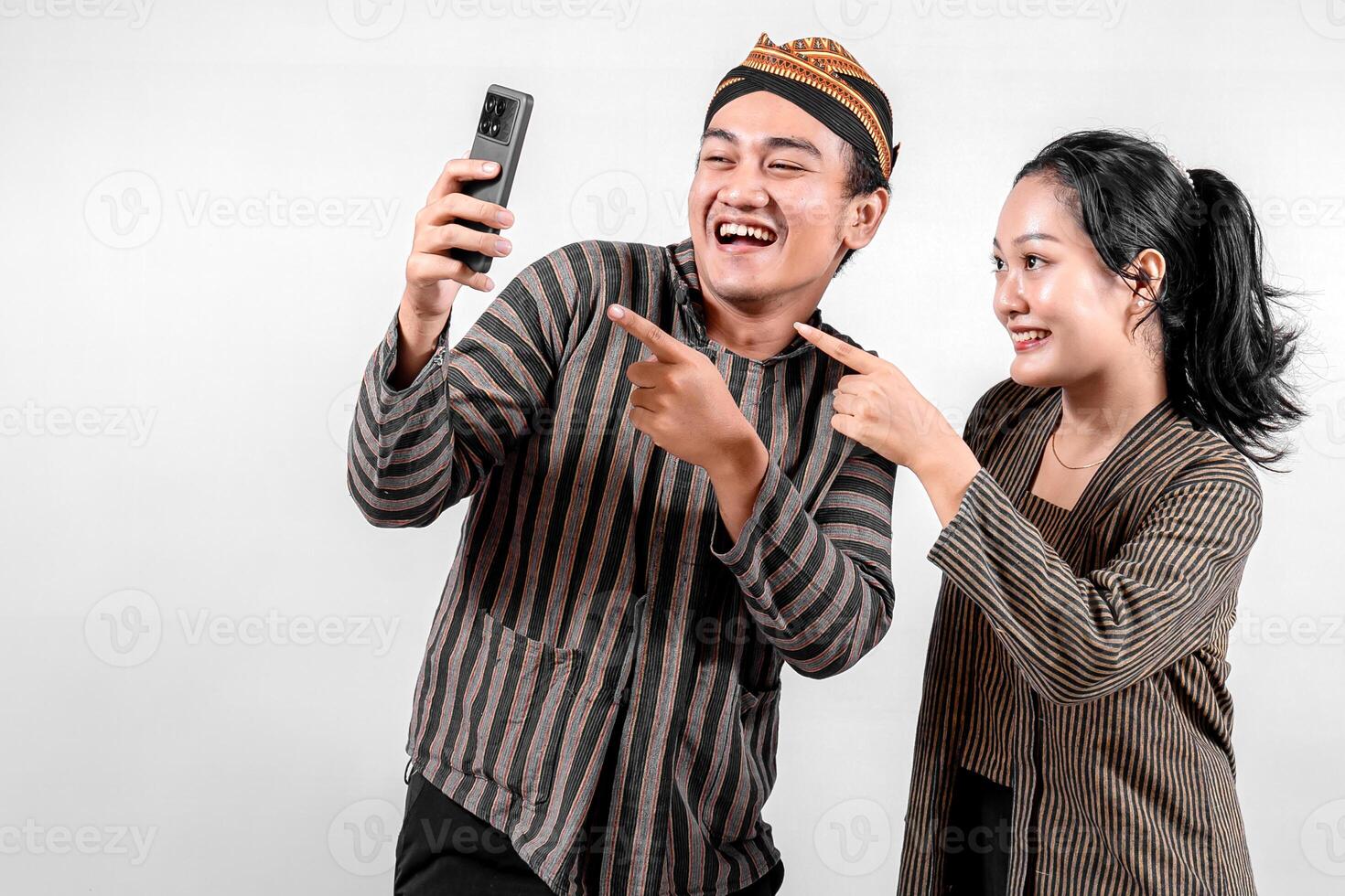 a Indonesian couple in traditional Javanese Lurik or Sorjan outfit taking a selfie together. Smiling, cheerful, and happy expression. Isolated on white background. photo