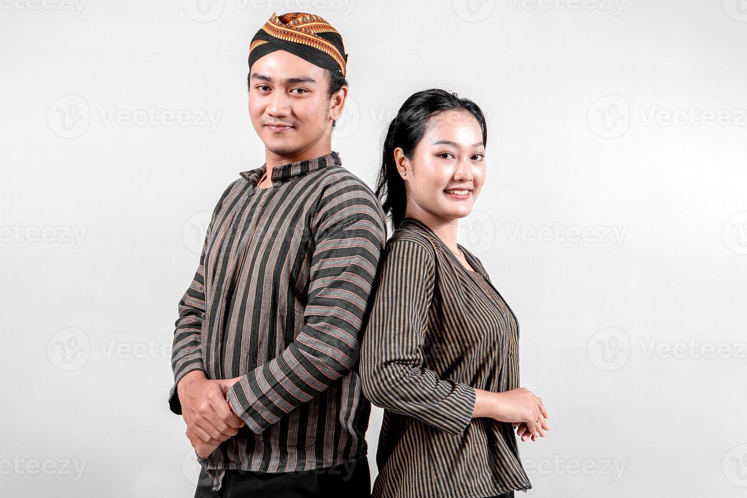 Indonesian man and a woman stand confidently back to back, wearing traditional lurik attire, exuding pride and happiness photo