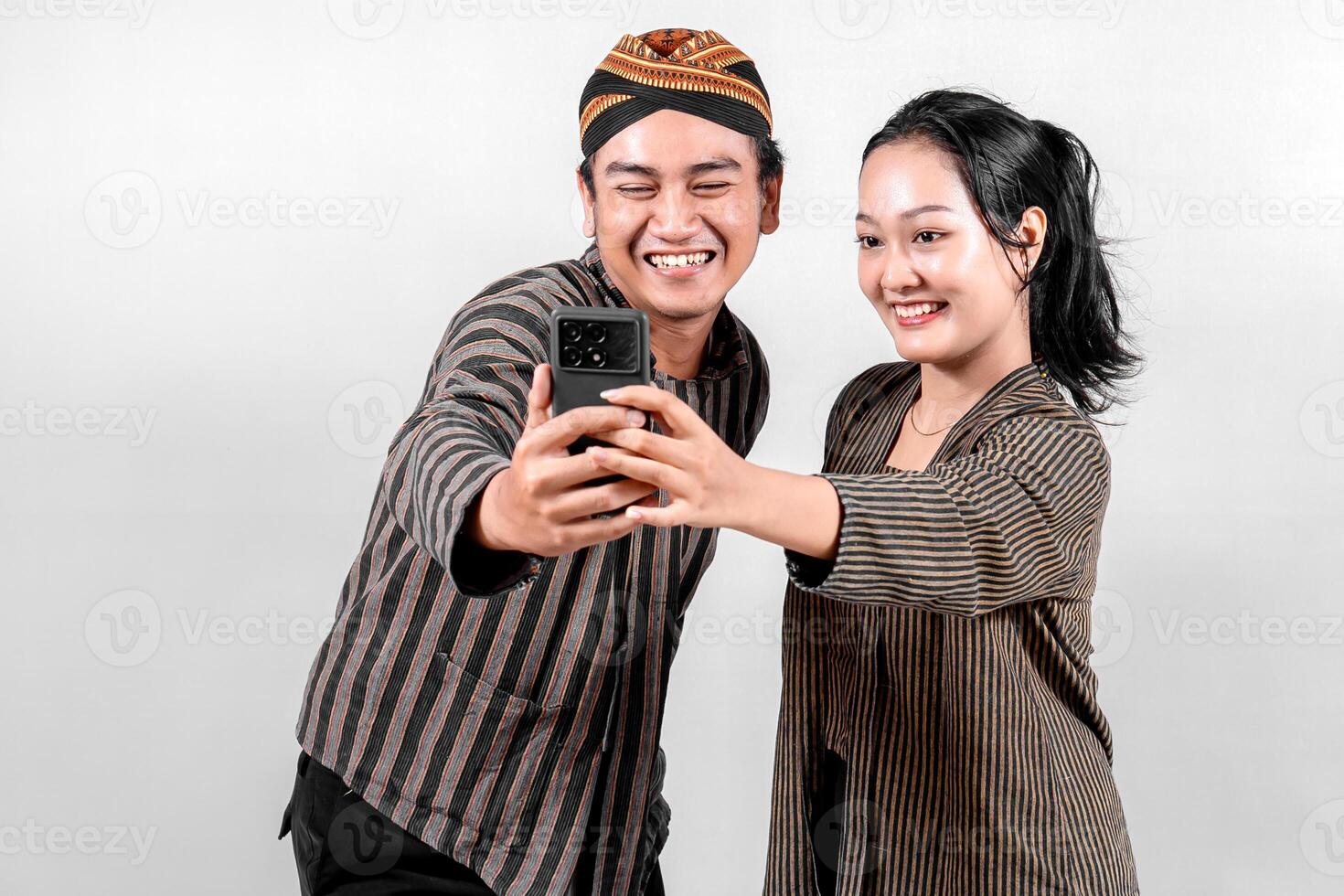 Indonesian couple in traditional Javanese Lurik or Sorjan clothing taking a selfie. Smiling, happy expression, cultural heritage fashion, isolated on white background. photo