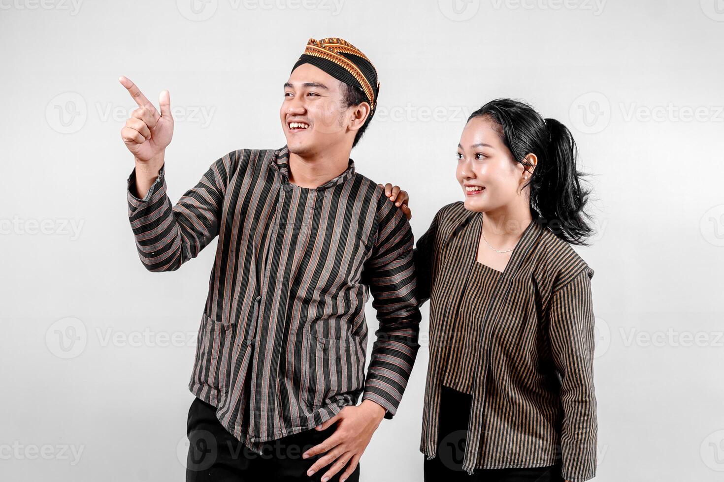 an Indonesian couple wearing traditional Lurik or Sorjan clothing, smiling and pointing. Javanese cultural outfit with striped pattern. Isolated on white background photo