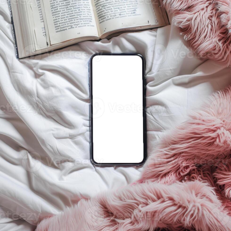 Blank iphone screen on a bed with a book and fluffy blanket photo