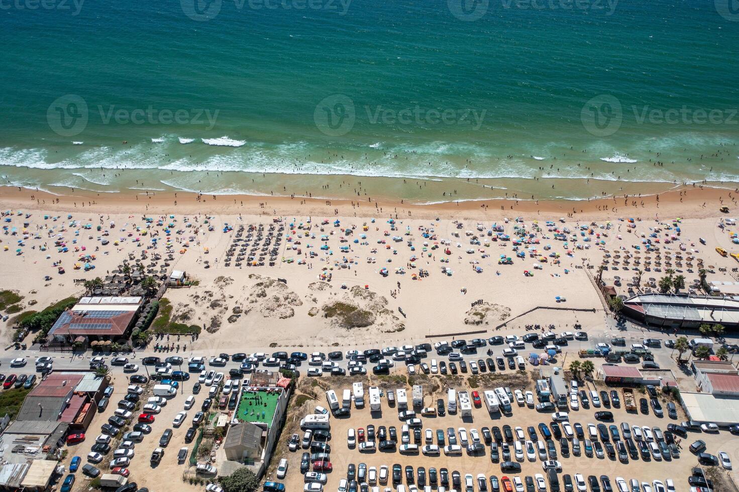 Crowded beach with car parking area and turquoise sea photo