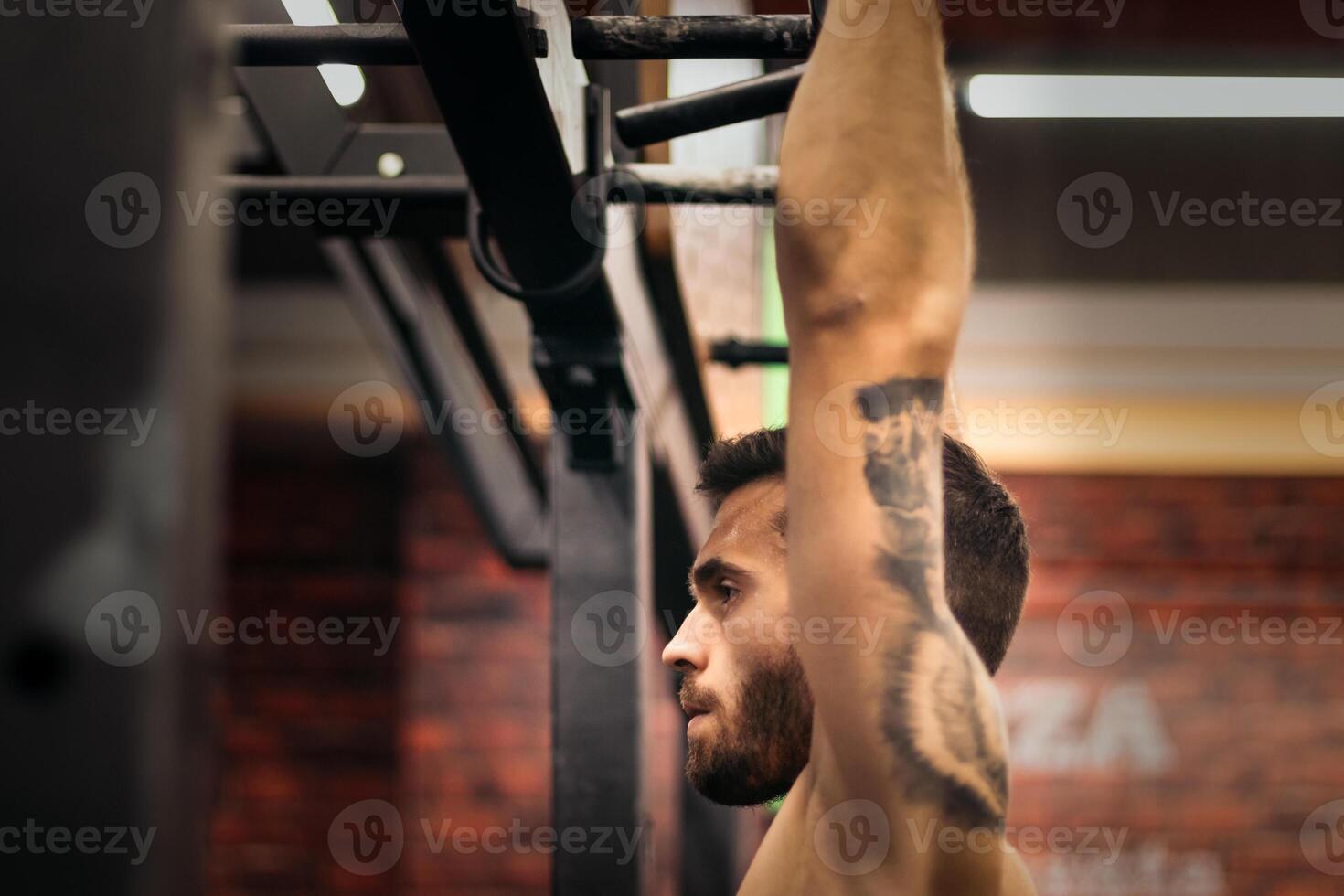 side view of a strong man doing pull ups in a gym. close-up photo