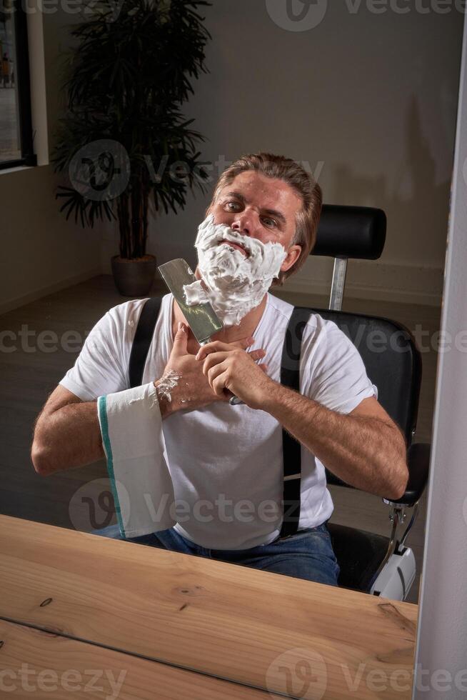 Adult barber shaving with knife in front of mirror photo
