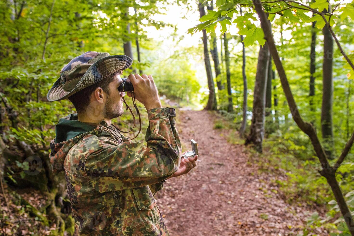 Soldier using binoculars and compass in forest photo
