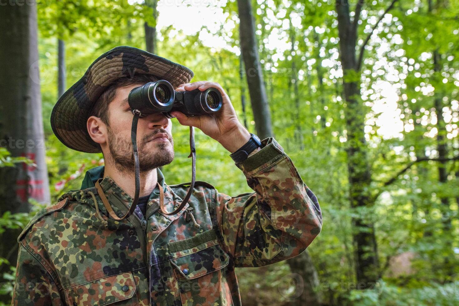 Soldier looking through binoculars while patrolling in forest photo