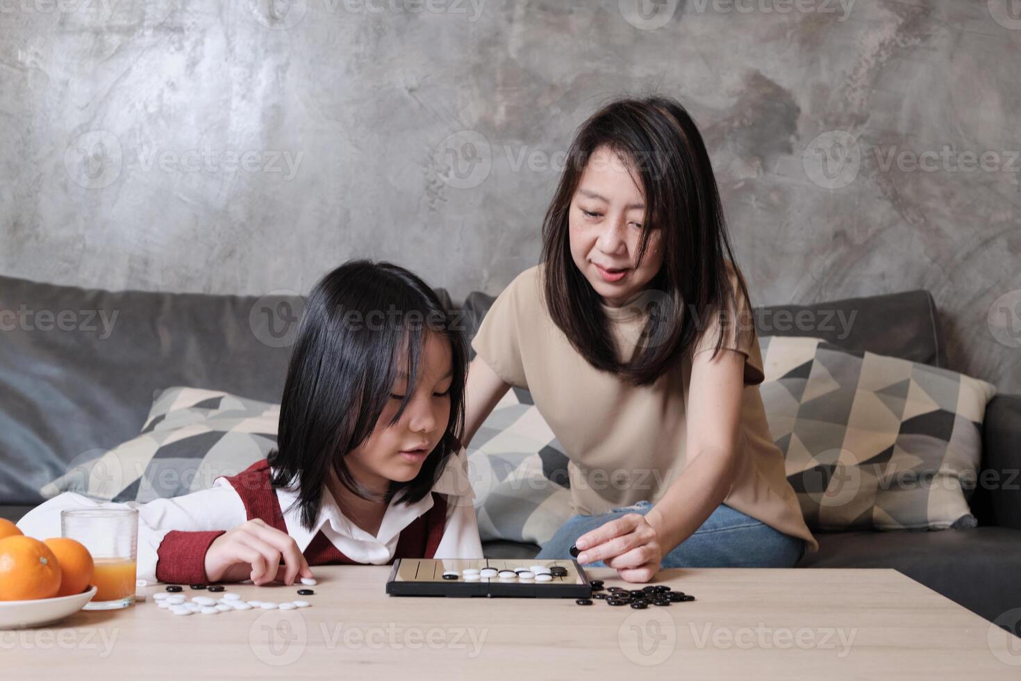 Asian mom, and kid fun playing Go, checkers board game on table in home family living room together with love and cheerful, happy weekend relaxing hobby of child and parent, concentrate and compete. photo