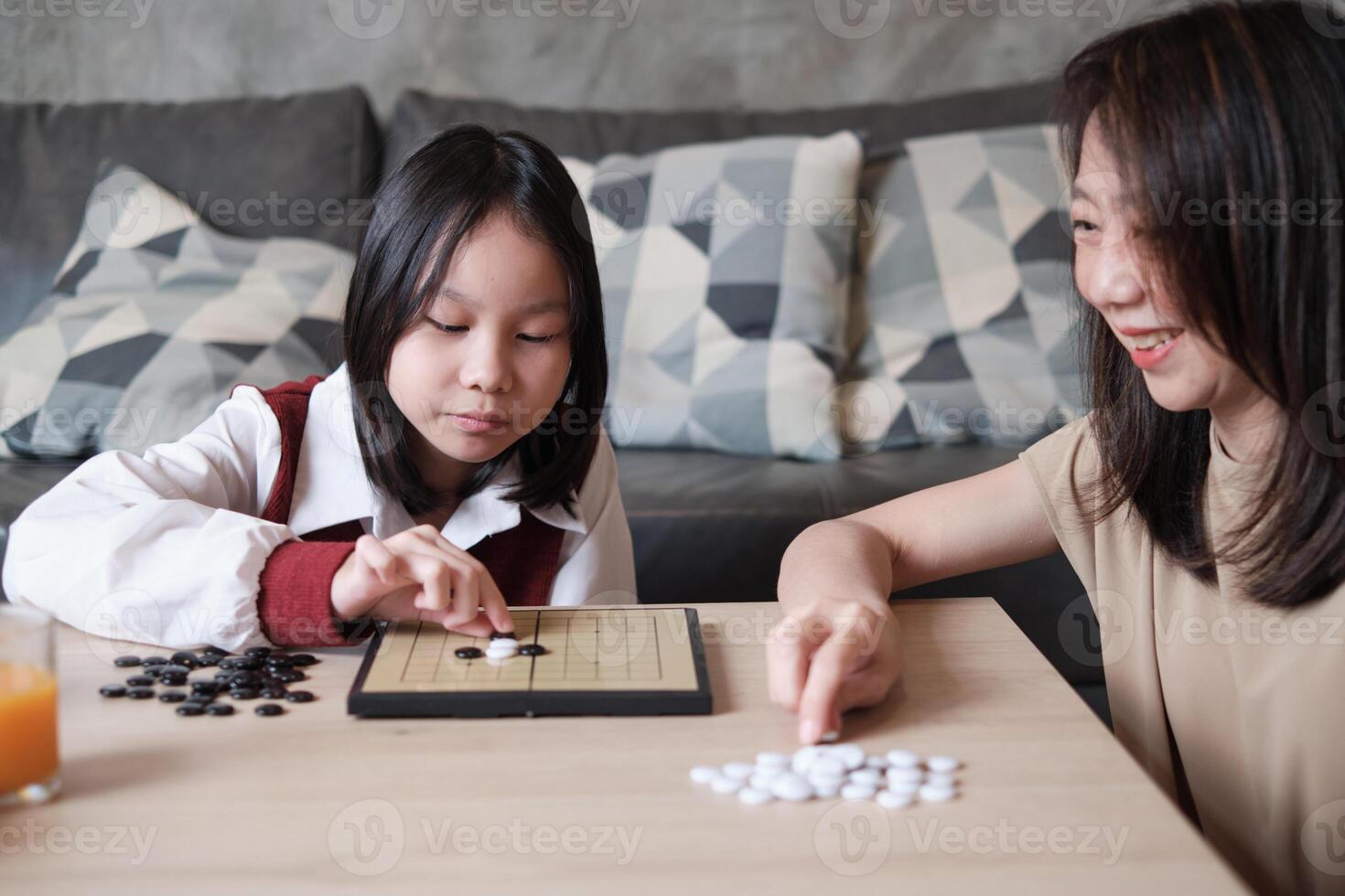Asian mum and kid are playing checkers board games on table in living room. photo