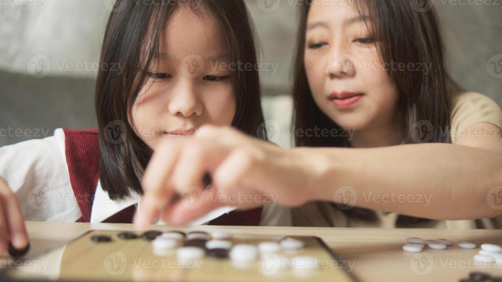 Asian family times, mom, and kid fun playing Go in close up shot, checkers board game on table in home living room together with love and cheerful, happy weekend relaxing hobby of child and parent. photo