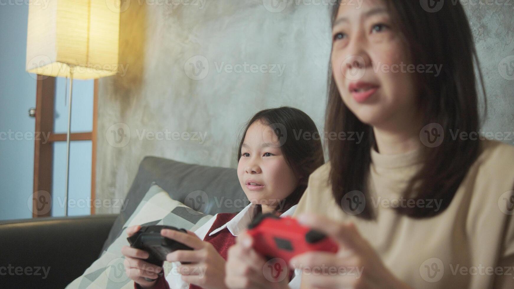 Asian family, mum, and kid fun playing console game with joy controllers on couch in living room together, enjoy and cheerful, happy weekend exciting hobby of child and parent, digital entertainment. photo