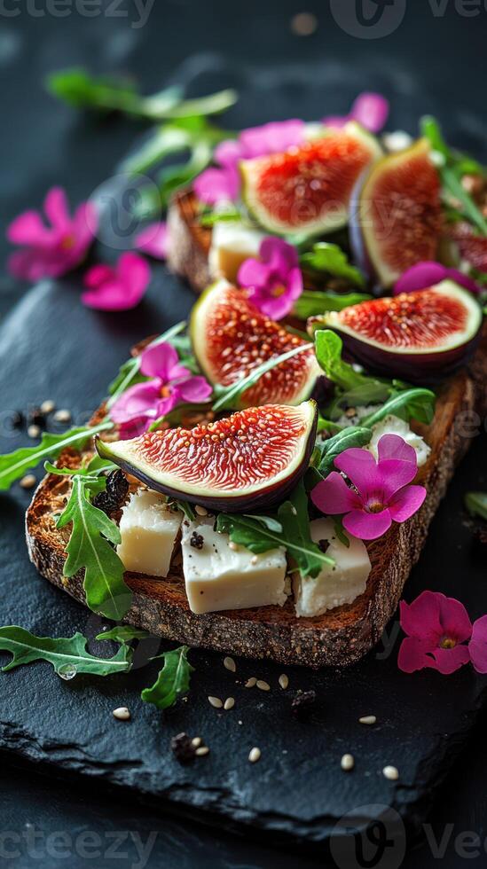 Fresh toast topped with figs, cheese, and arugula garnished with flowers on a dark slate plate photo