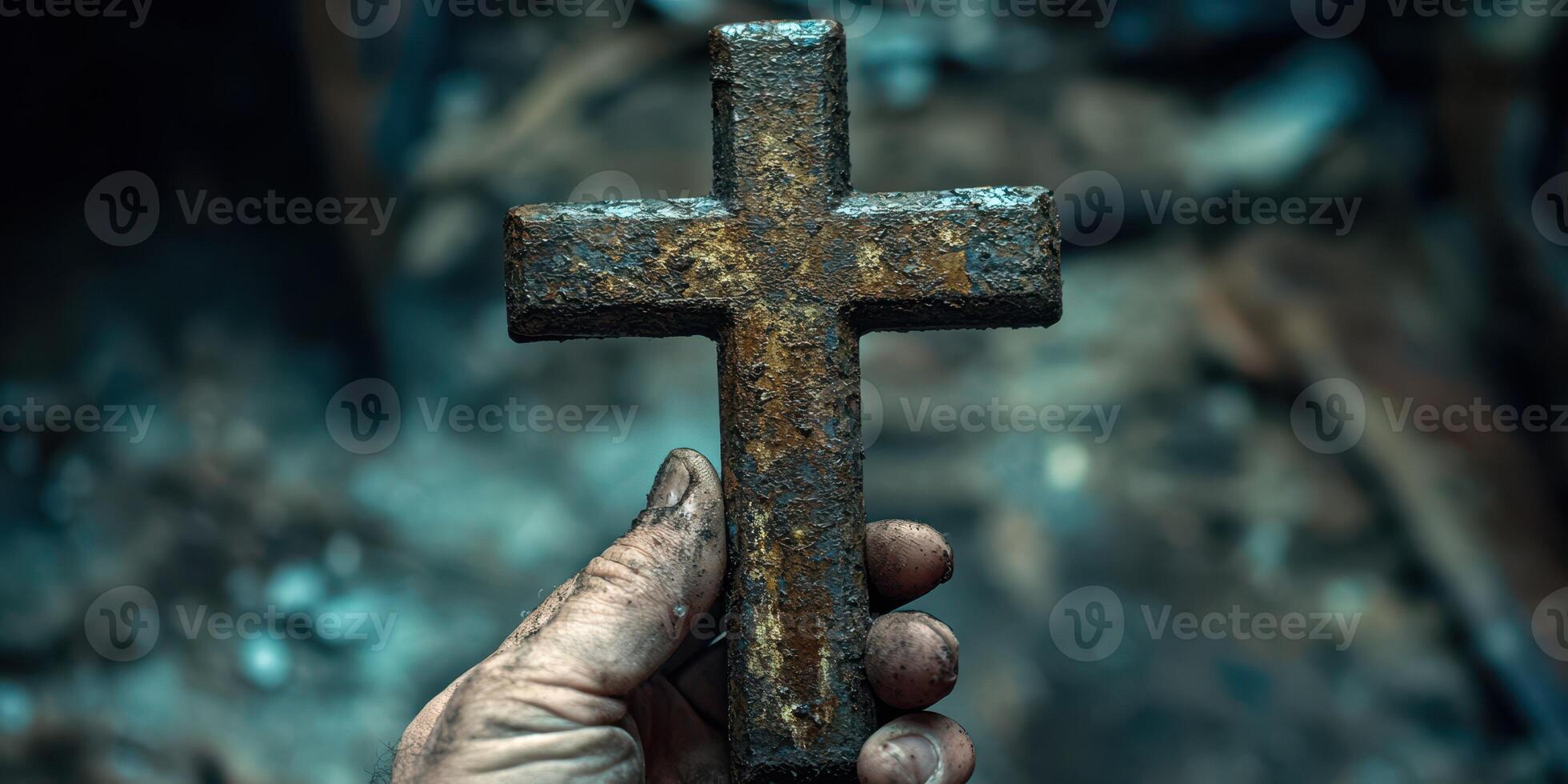 Rusty cross held in a hand amidst remnants of a fire-lit environment in a somber setting photo