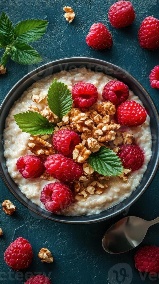 Creamy oatmeal topped with fresh raspberries and walnuts in a dark bowl on textured surface photo