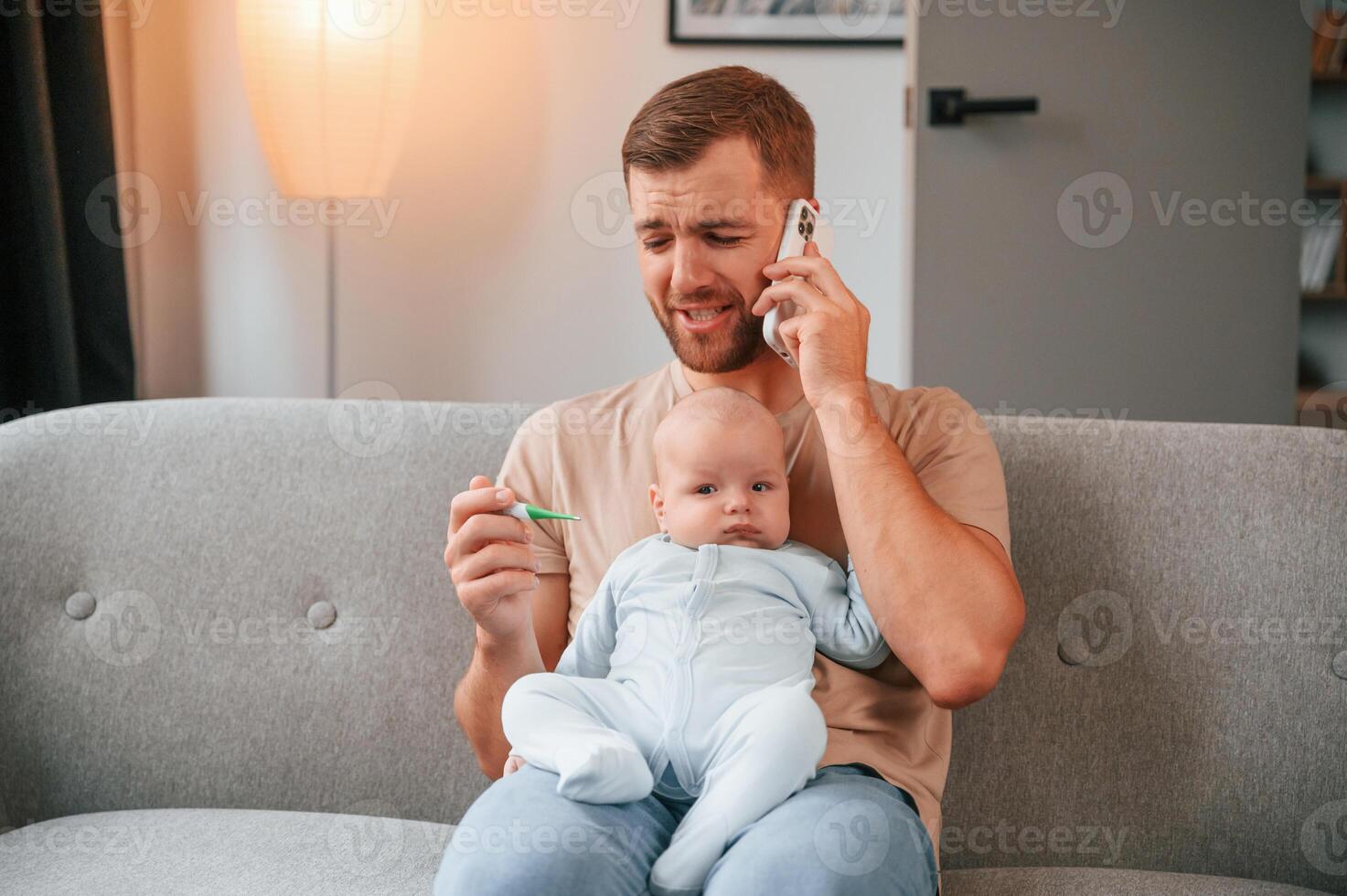 Calling doctor. With thermometer.. Father with his newborn baby is indoors. Conception of single dad photo