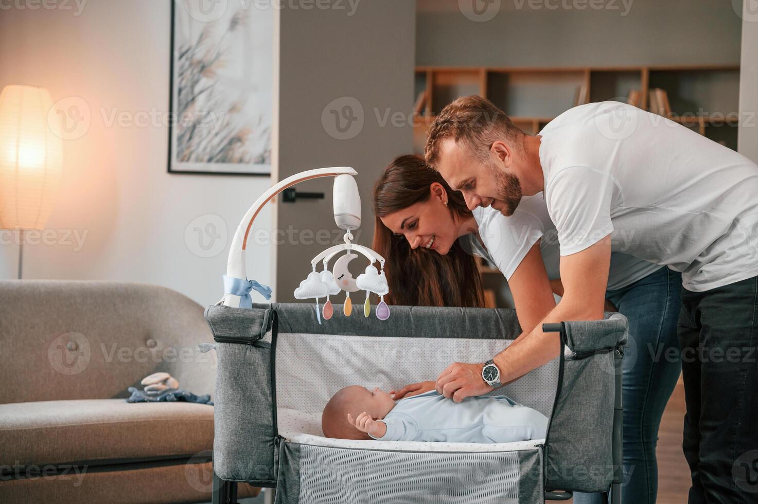 Looks down ,at the kids. Lovely couple taking care of newborn baby indoors at domestic room photo
