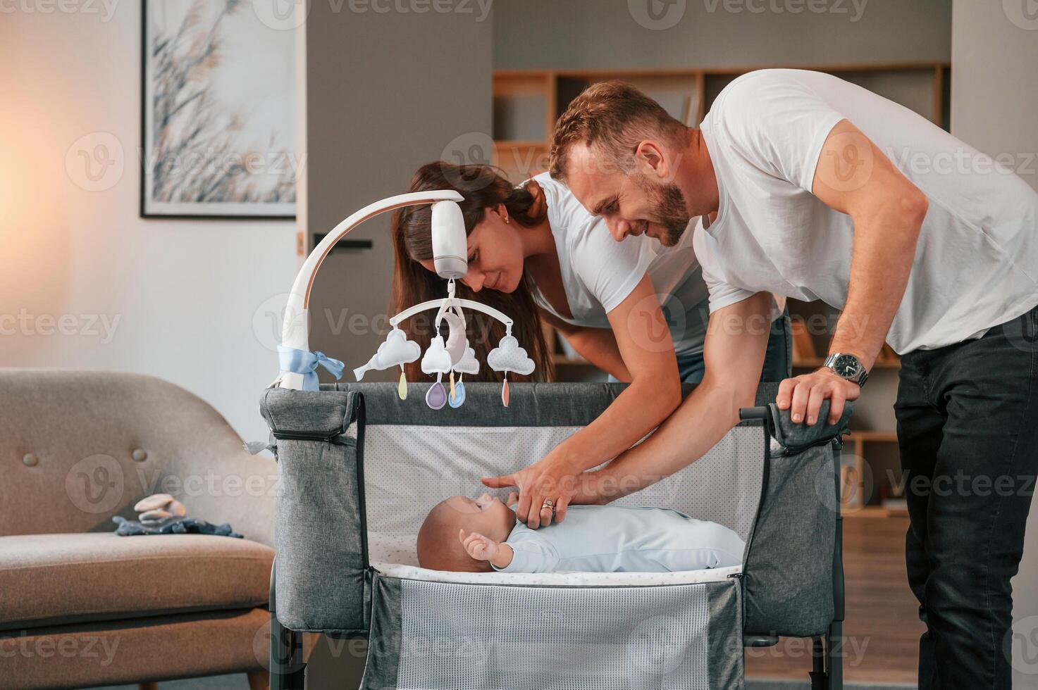 Looks down, at the kids. Lovely couple taking care of newborn baby indoors at domestic room photo
