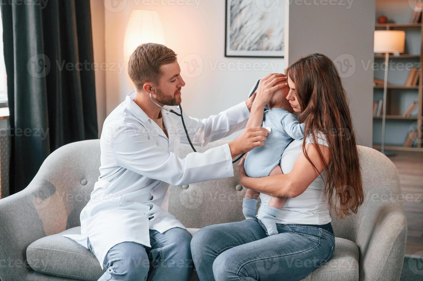 Using stethoscope. Male, doctor, is taking care of woman's newborn baby indoors photo