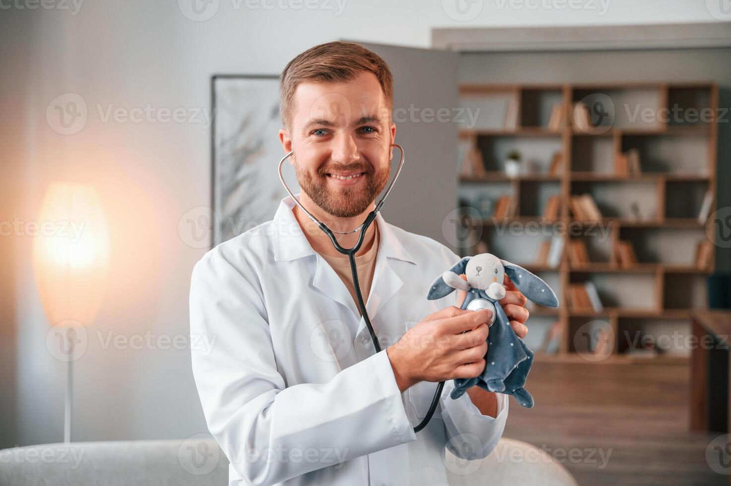 Portrait of male doctor in, white coat that holding stethoscope with toy photo