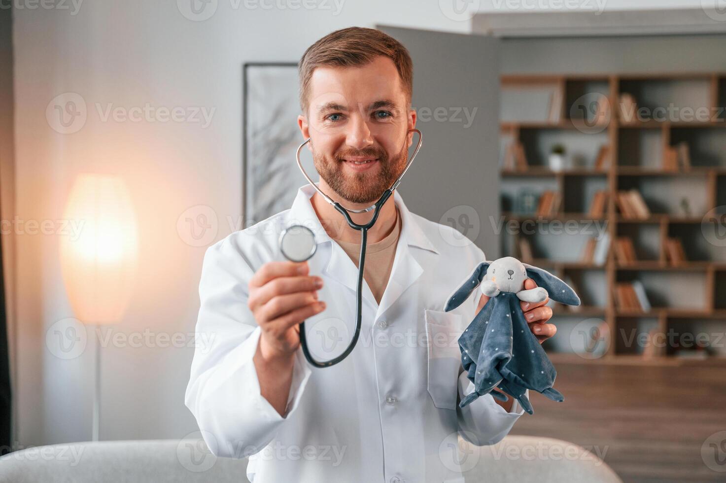 Portrait, of male doctor in white coat that holding stethoscope with toy photo