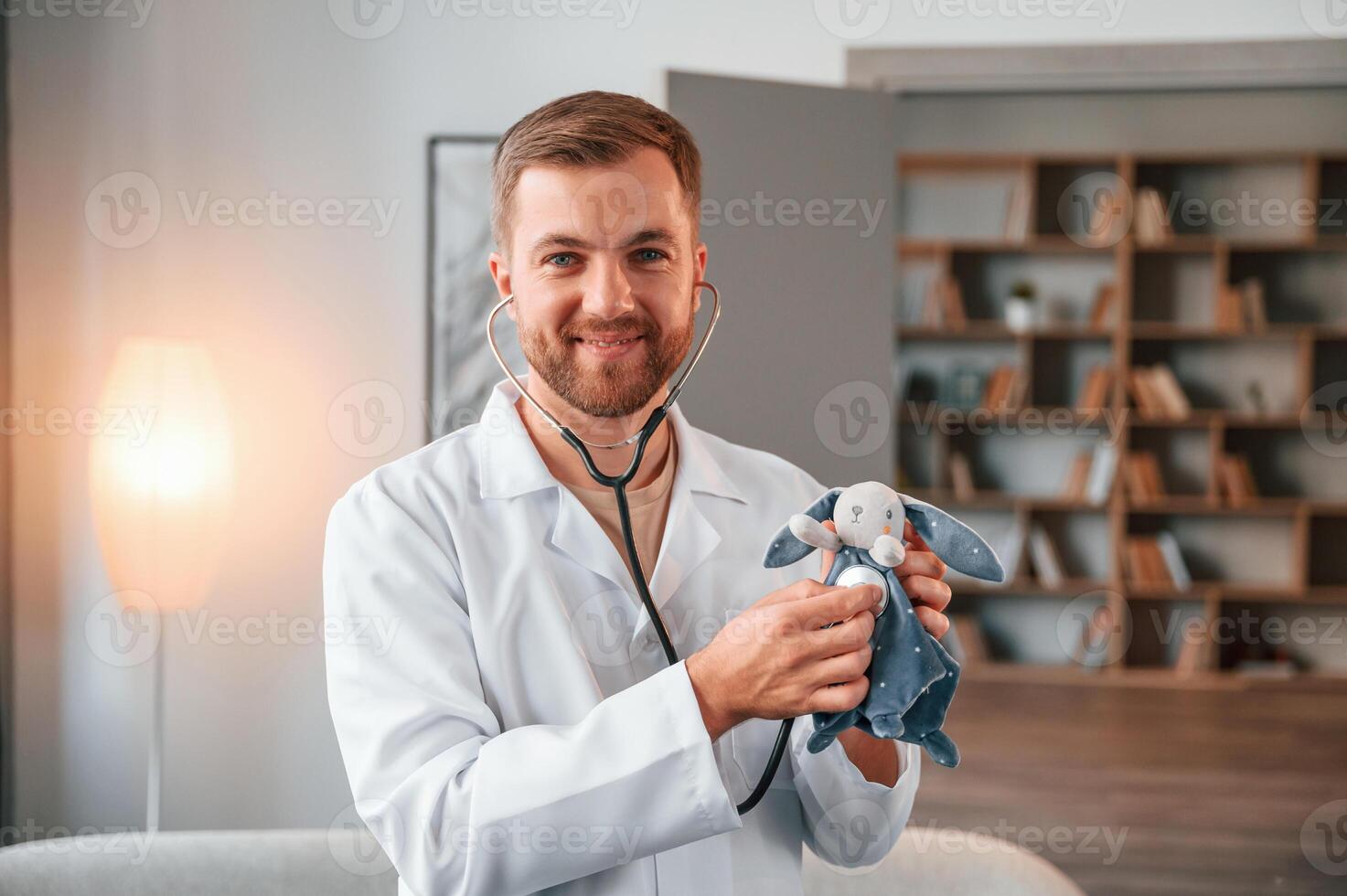Portrait of male doctor in white coat that holding stethoscope with toy photo