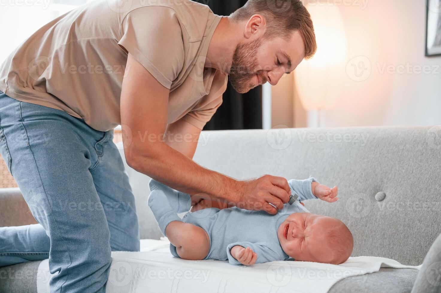 Baby is crying, man tries to give him medicine. Father is indoors. Conception of single dad photo