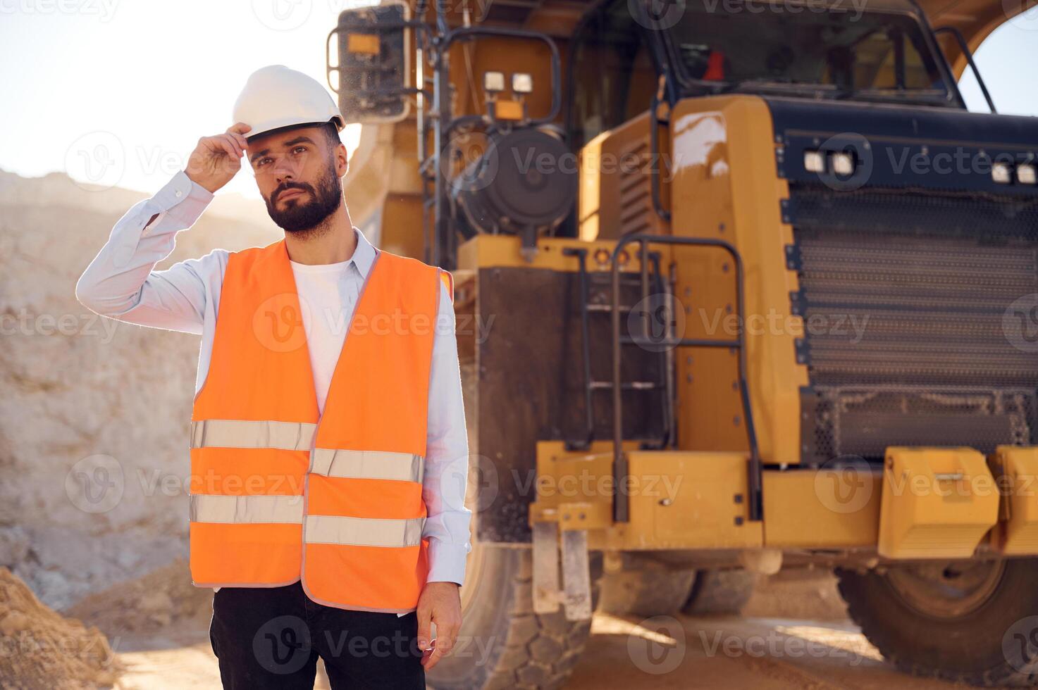 Beautiful man, in uniform is working in the quarry at daytime. With haul truck photo