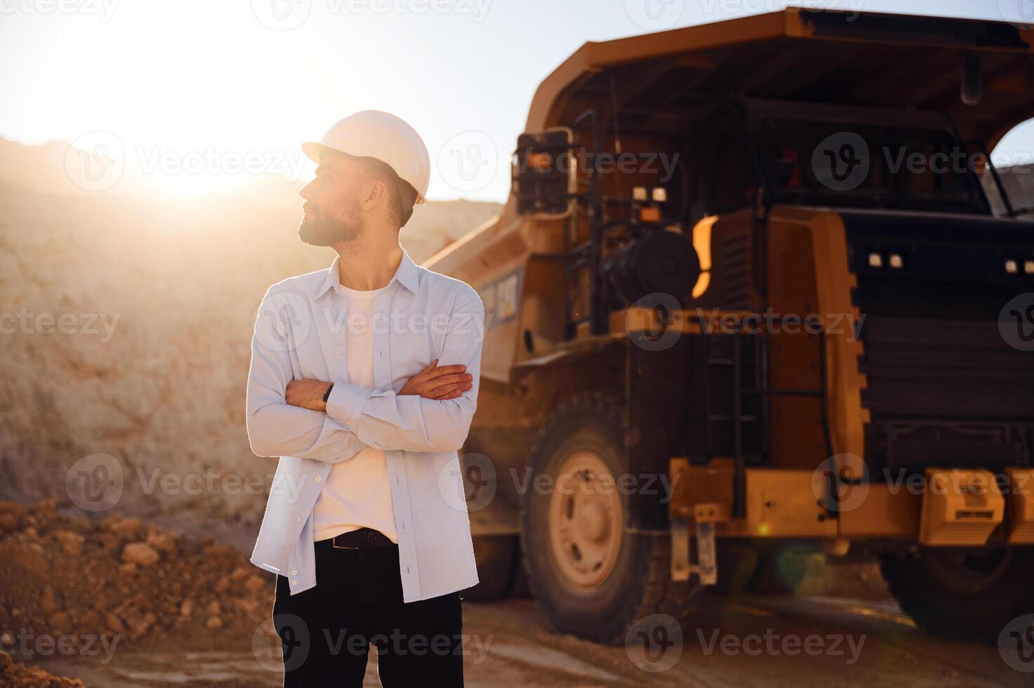 Standing against ,big haul truck. Man in uniform is working in the quarry at daytime photo