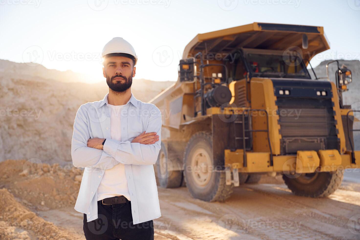 Standing against big haul truck. Man in uniform ,is working in the quarry at daytime photo