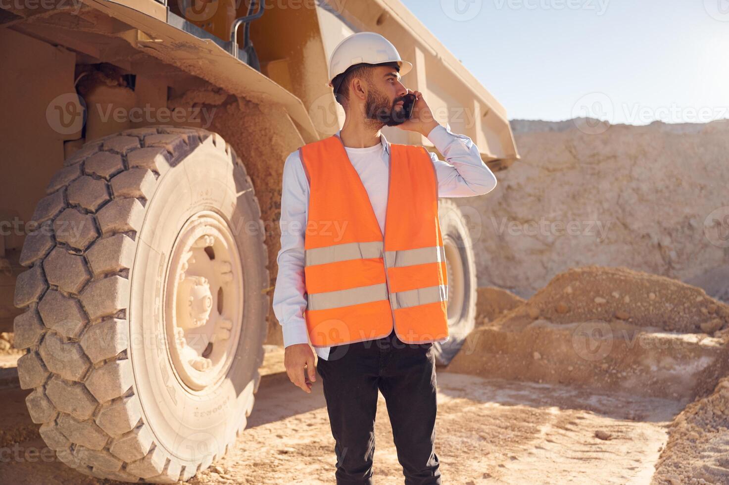 Using smartphone. Man, in ,uniform is working in the quarry at daytime photo