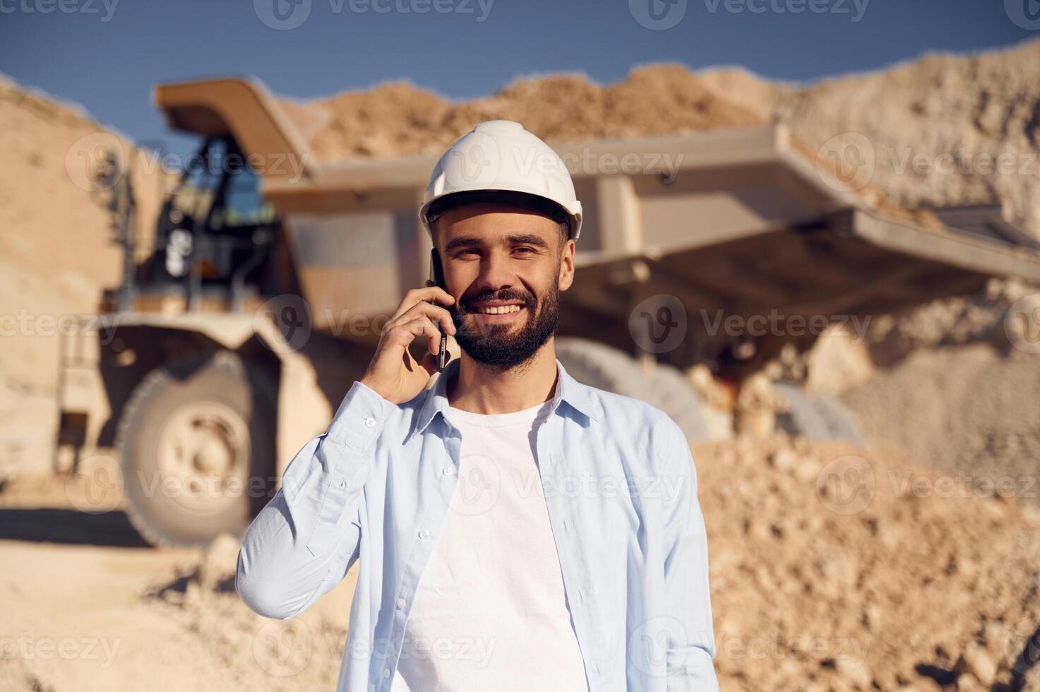 Engineer is with the phone. Man, in uniform is working in the quarry at daytime photo