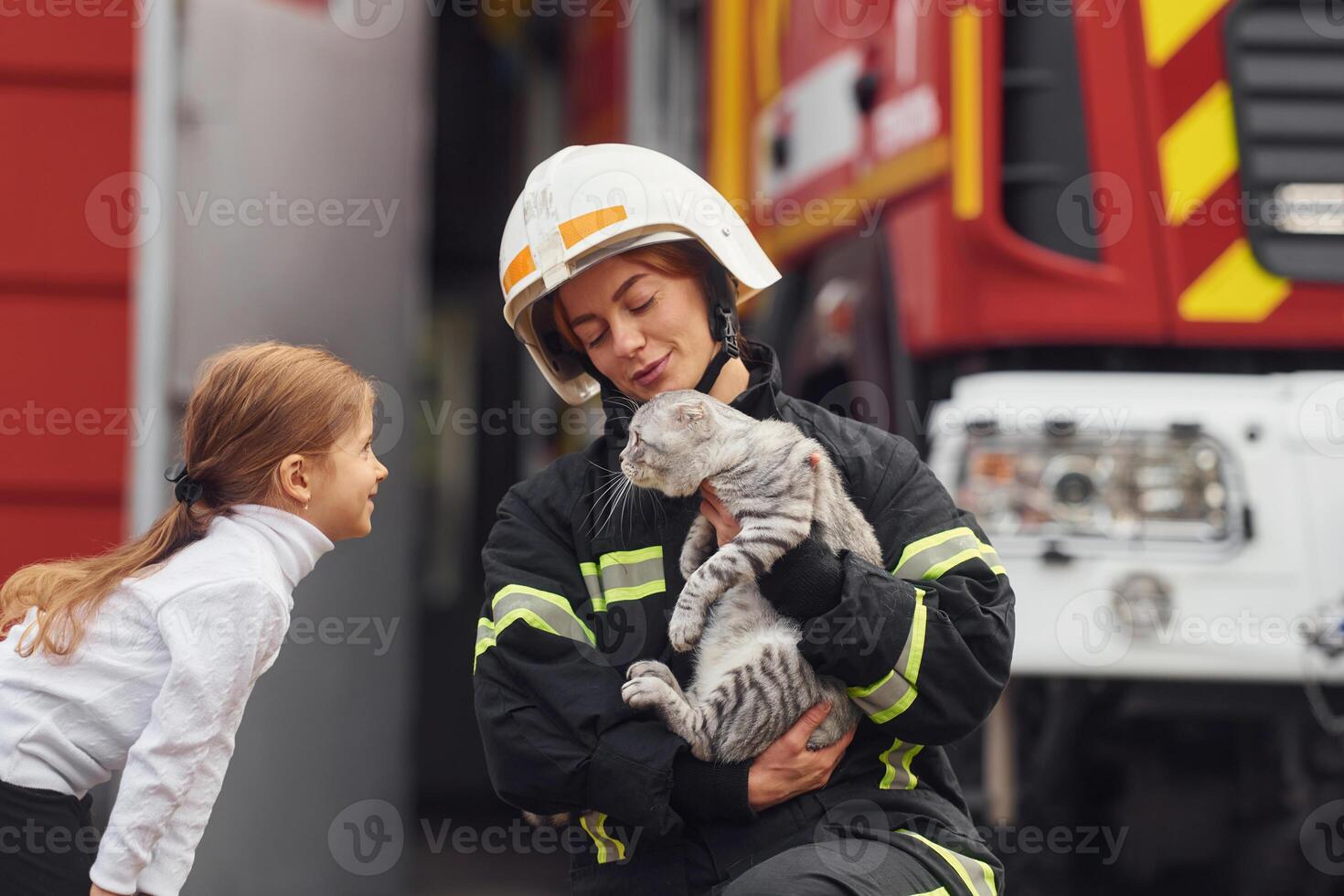 Cute, scottish fold cat is in the hands. Firefighter woman in uniform is with a little girl photo