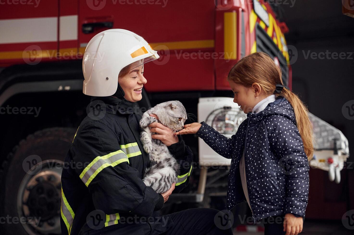 Cute ,scottish fold cat is in the hands. Firefighter woman in uniform is with a little girl photo