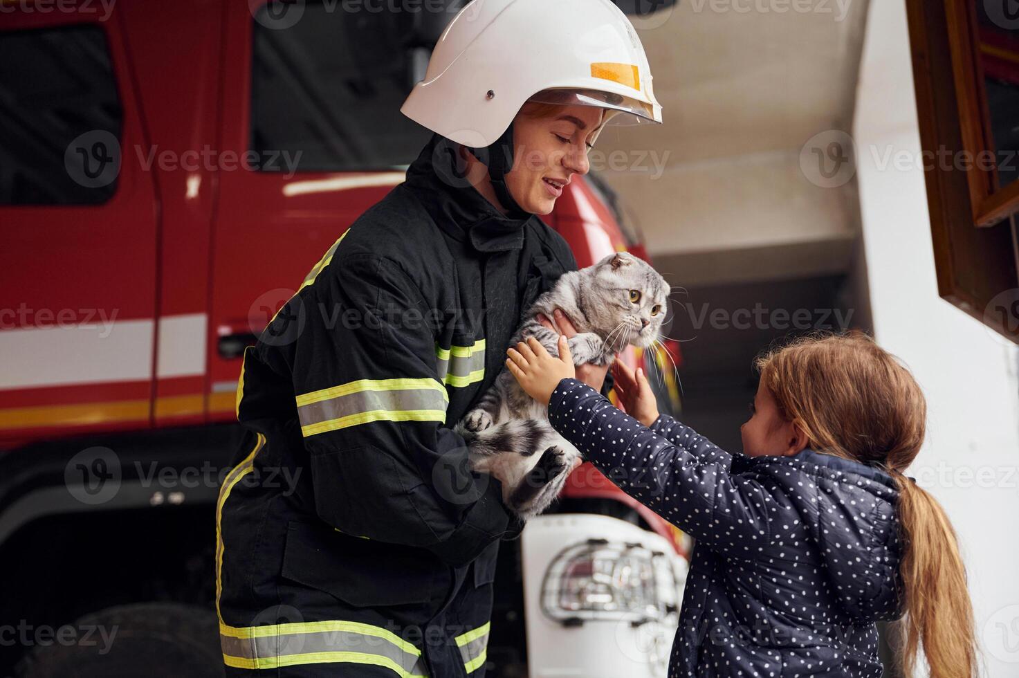 Giving scottish fold ,cat to the owner. Firefighter woman in uniform is with a little girl photo