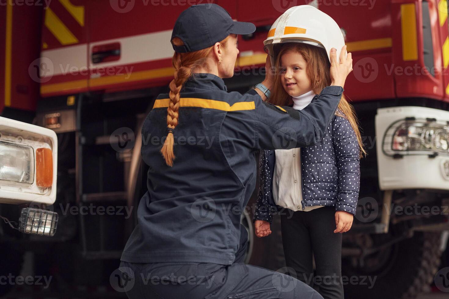 Wearing ,the helmet. Firefighter woman in uniform is with a little girl photo