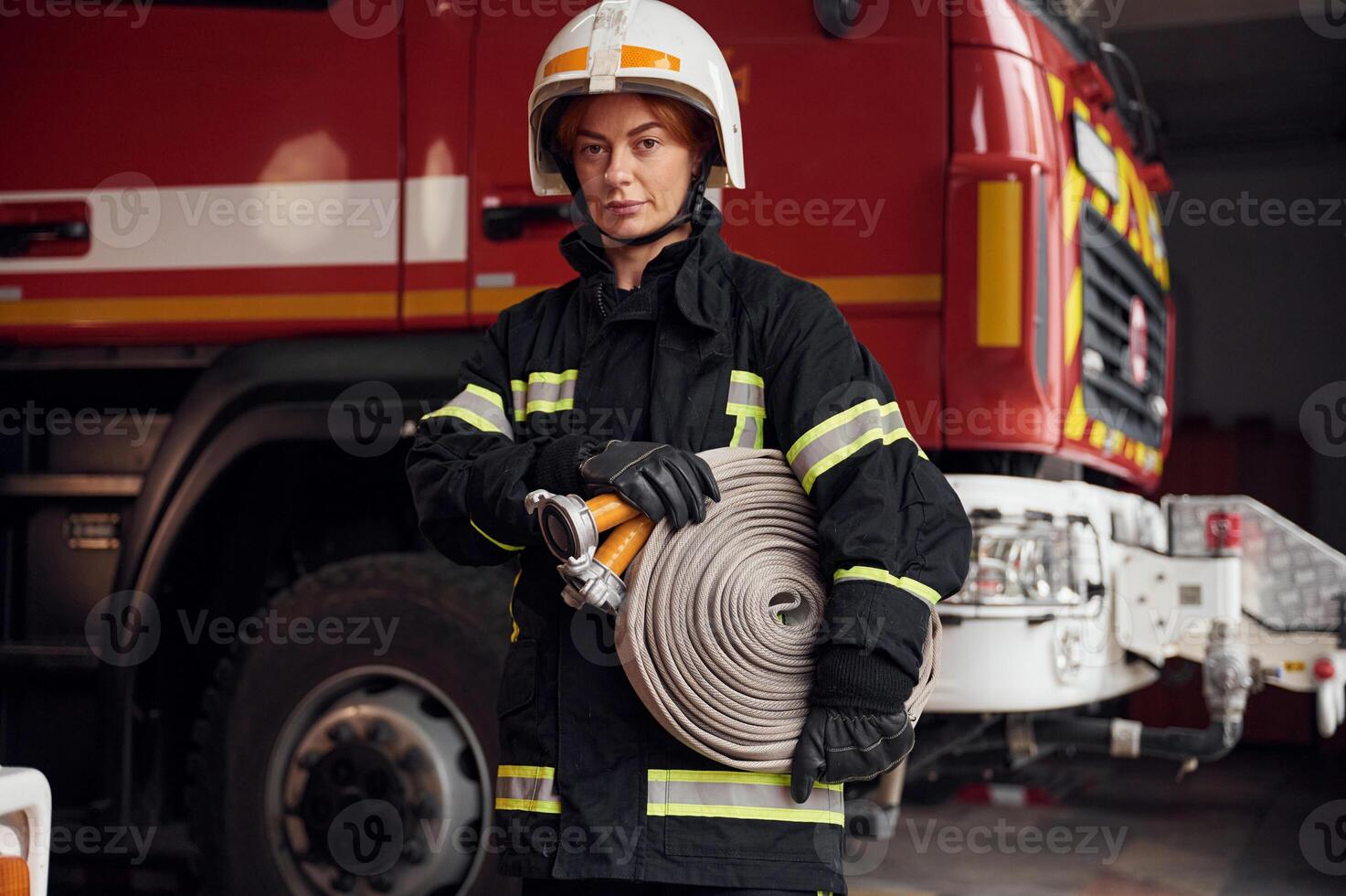 Grey, colored fire hose is in the hands.. Woman in uniform is at work in department photo