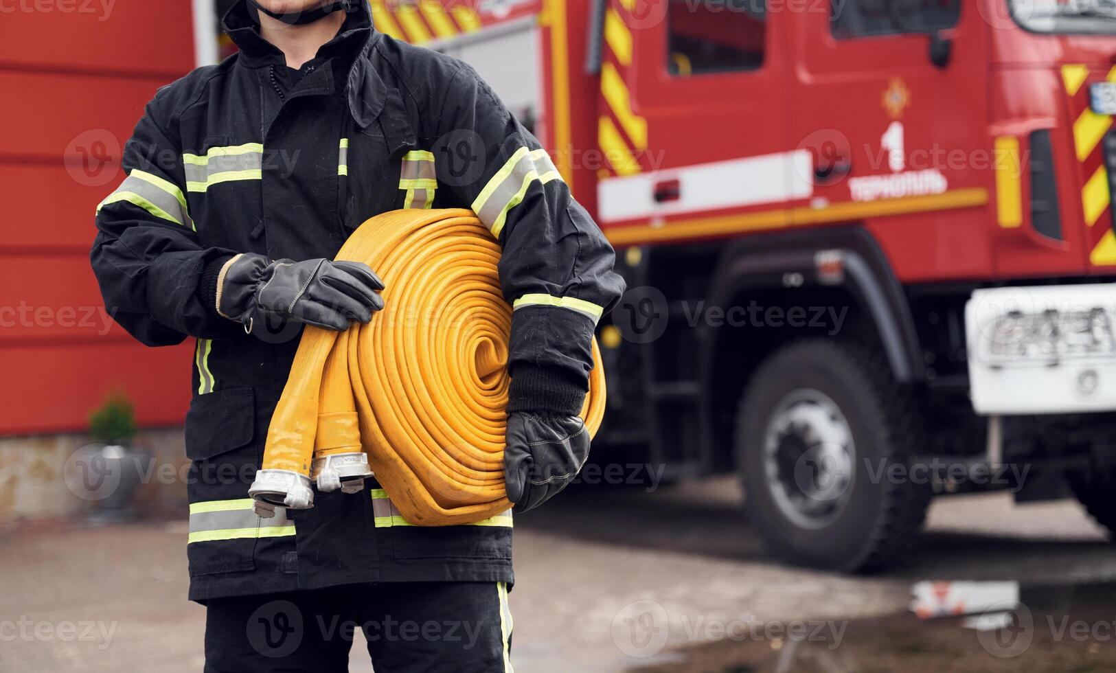 Outside, near truck and with fire hose in hands. Woman in uniform is at work in department photo