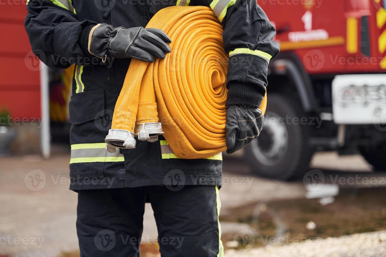 Outside ,near truck and with fire hose in hands. Woman in uniform is at work in department photo