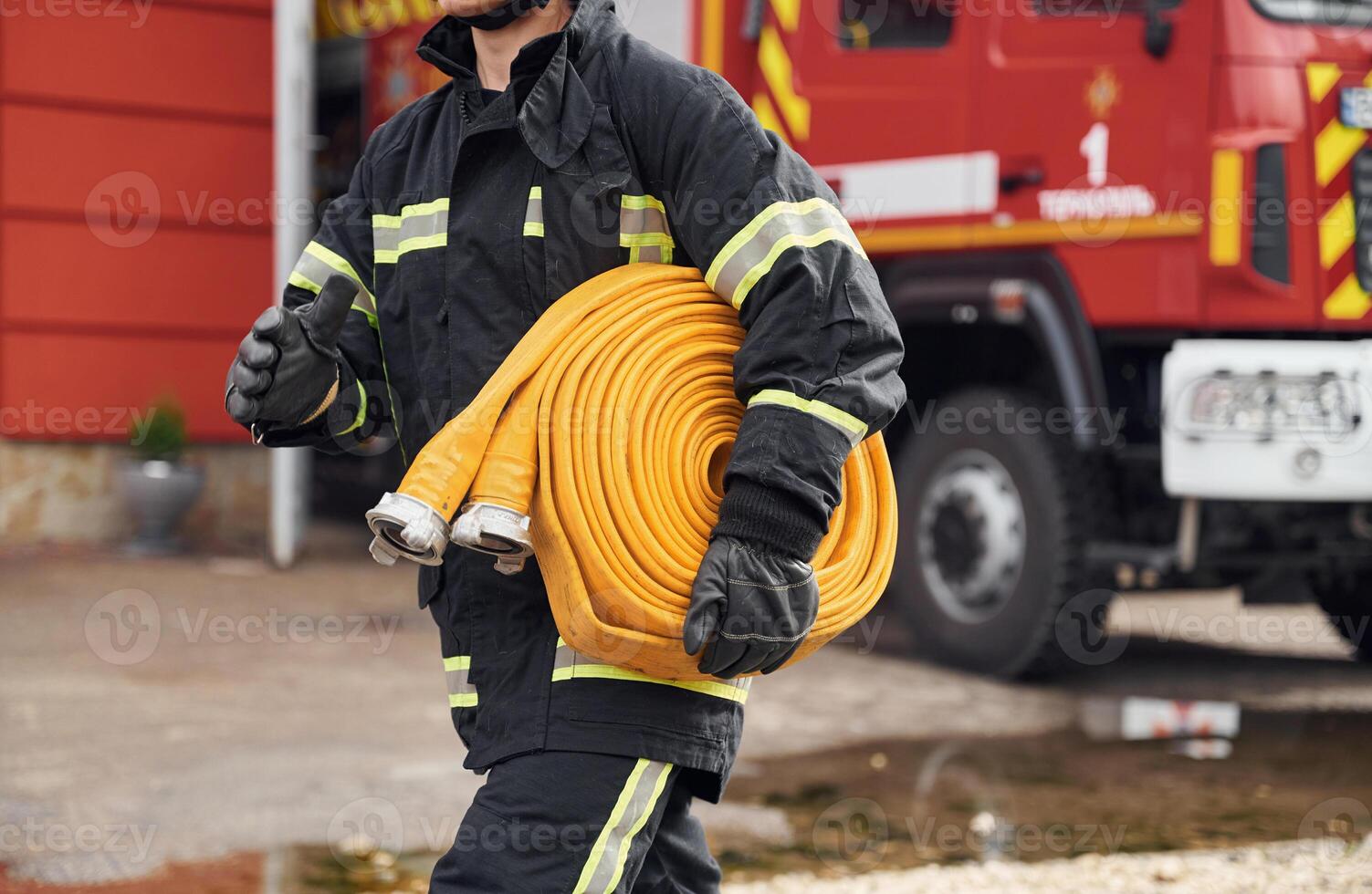 Outside near, truck and with fire hose in hands. Woman in uniform is at work in department photo