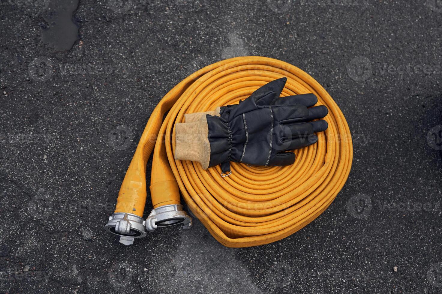 Top view of yellow fire hose with black gloves on it on the ground photo