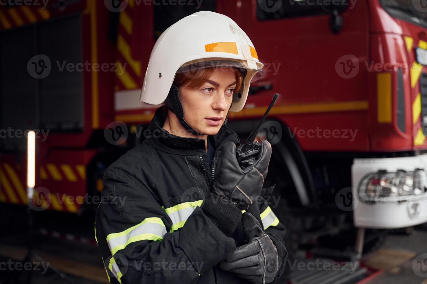 Talking by using radio transmitter. Woman firefighter in uniform is at work in department photo