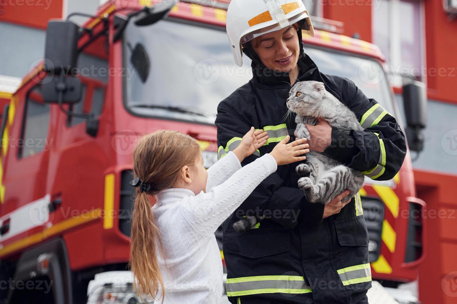 Cute scottish fold cat is in the hands. Firefighter woman in uniform is with a little girl photo