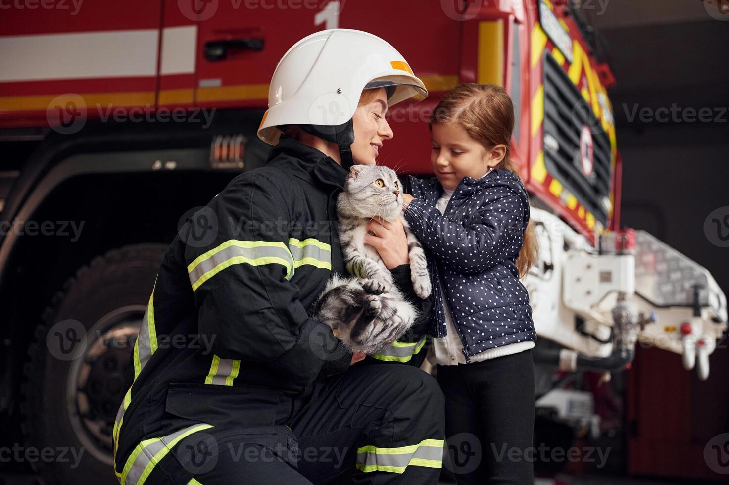 Cute scottish fold cat is in the hands. Firefighter ,woman in uniform is with a little girl photo