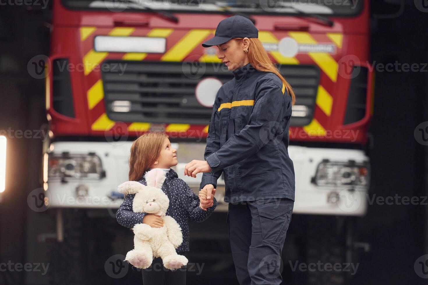 Against big truck.. With ,bunny toy. Firefighter woman in uniform is with a little girl photo