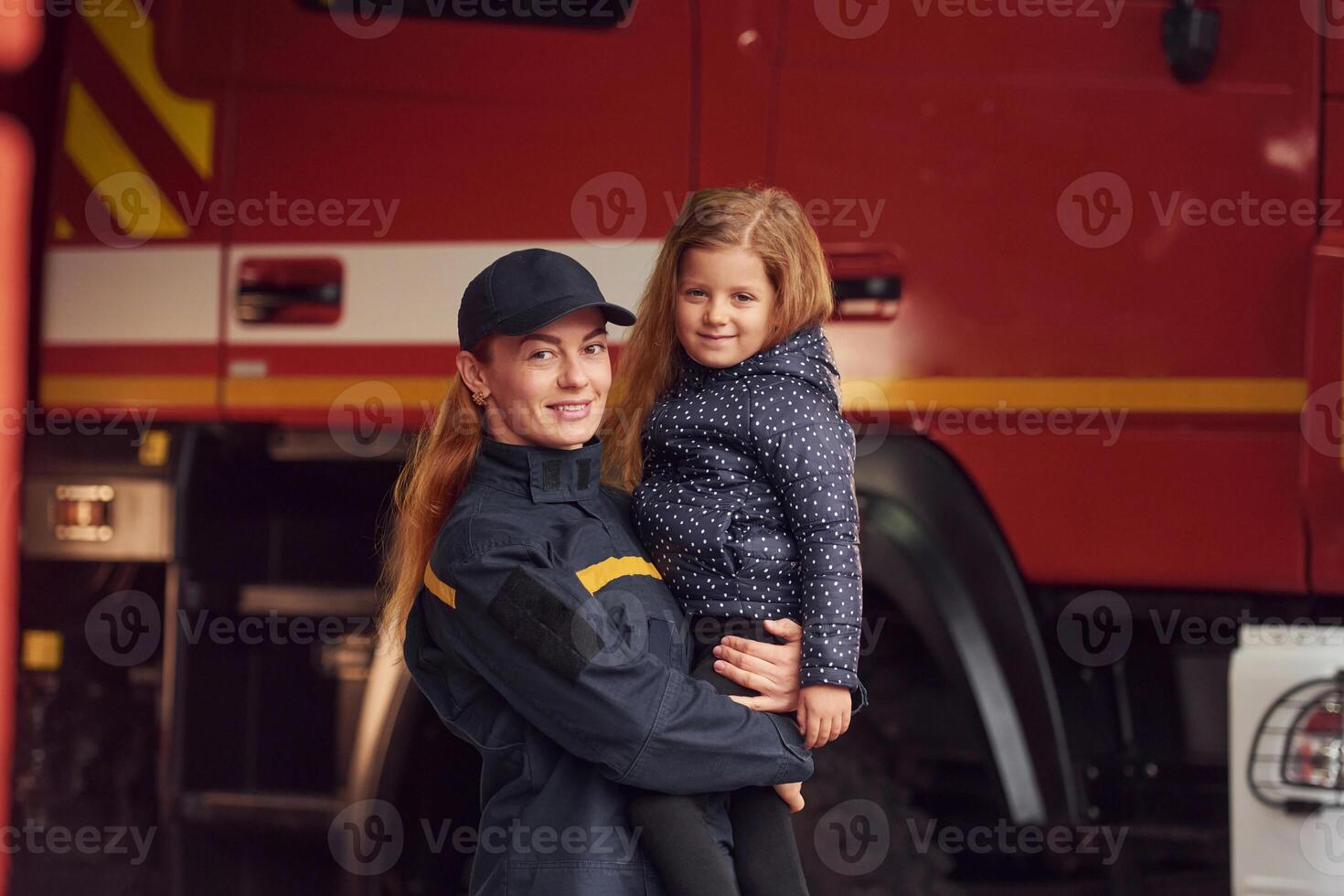 Firefighter woman ,in uniform is holding a little girl in the hands photo