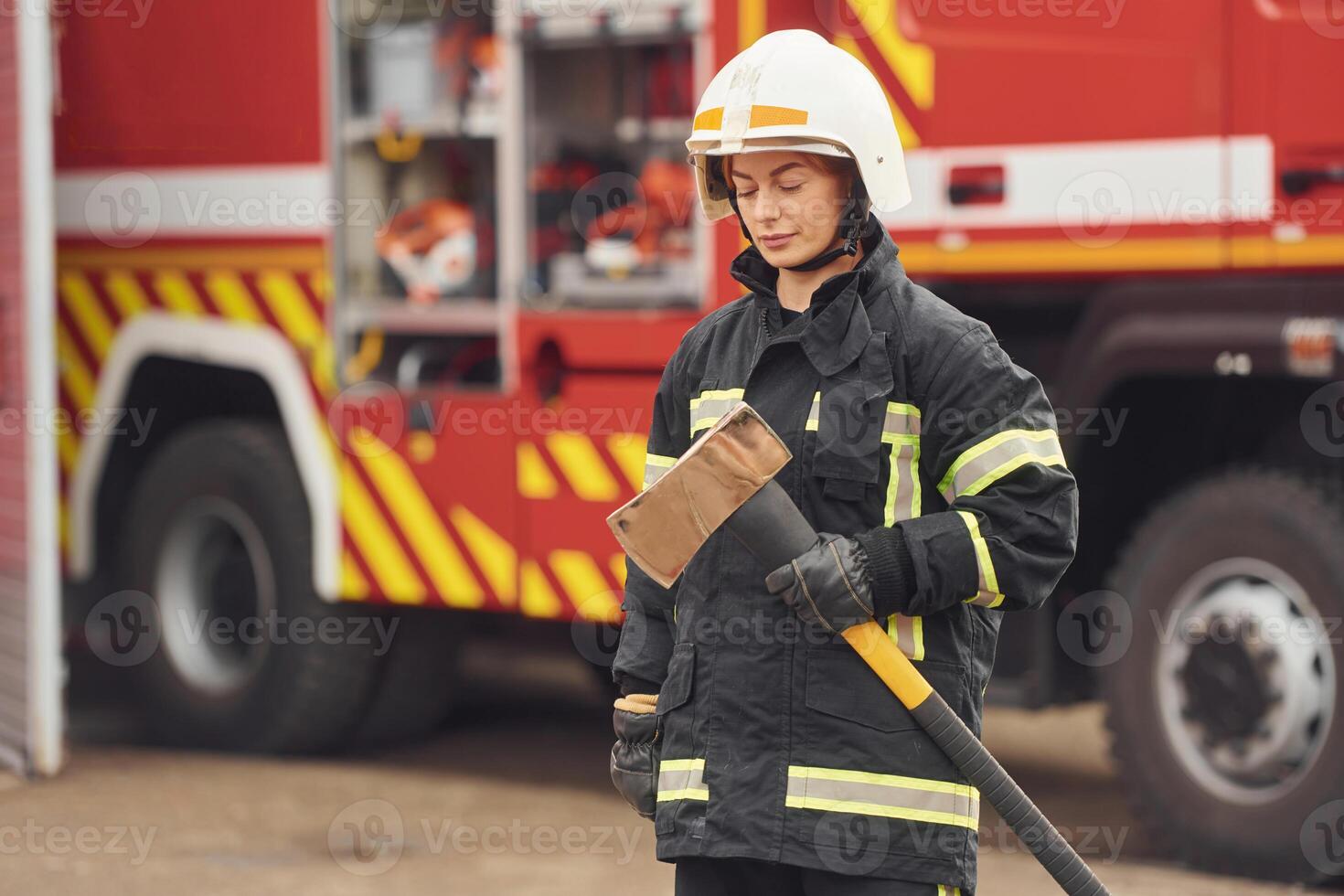 Standing with axe in ,hands against truck. Woman firefighter in uniform is at work in department photo