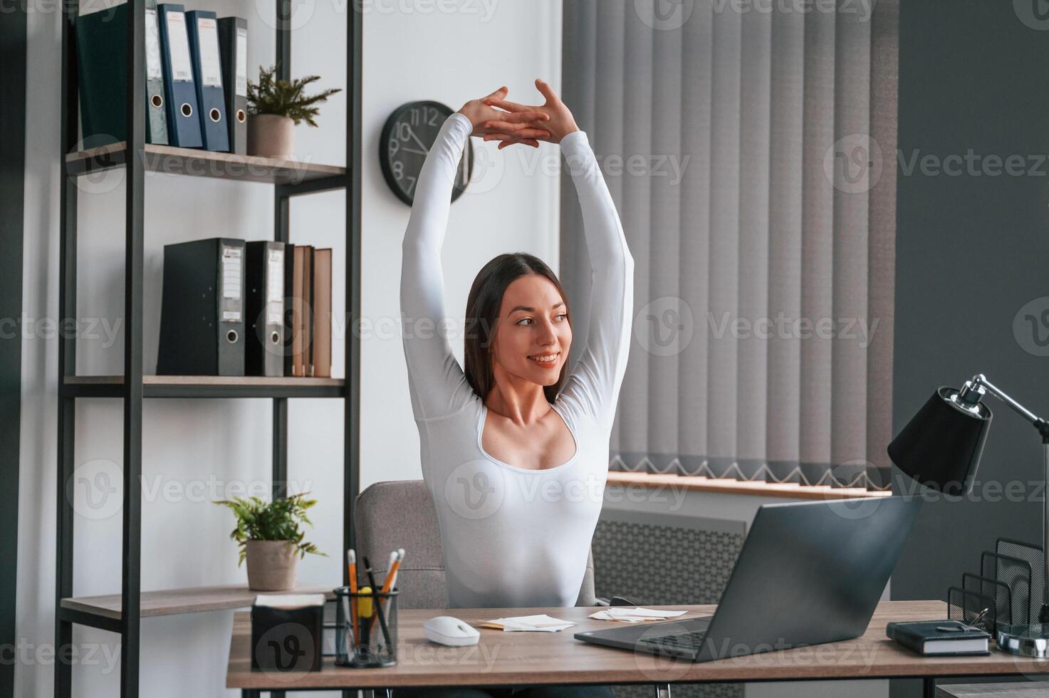 Takes, a break, stretches her hands. Young beautiful woman in white clothes is in the office photo