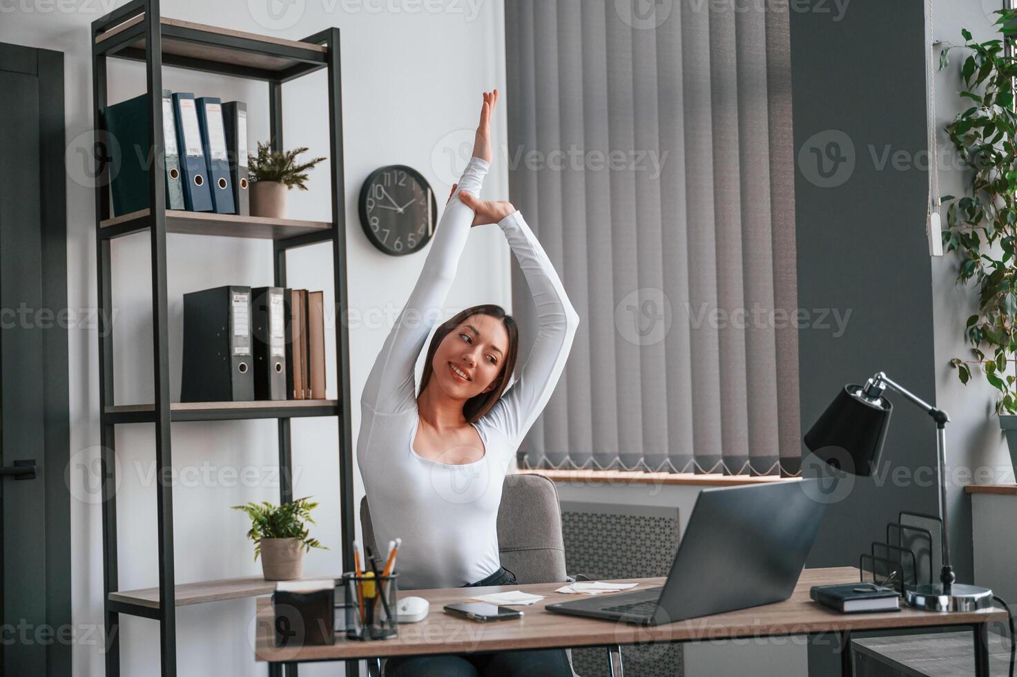 Takes a break,, stretches her hands. Young beautiful woman in white clothes is in the office photo