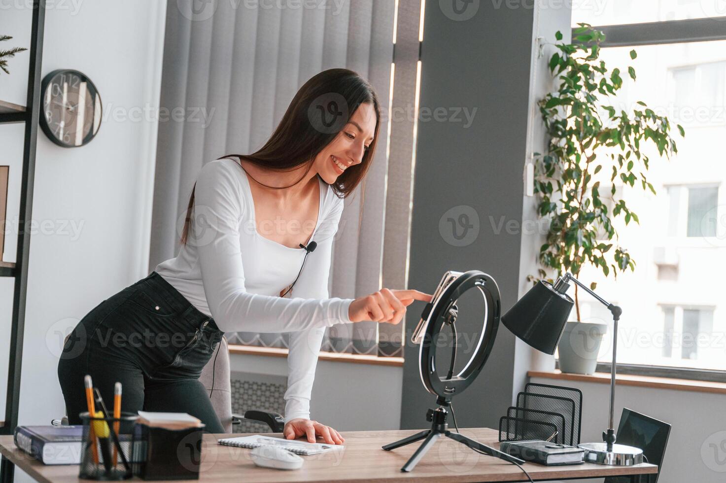 Setting, up the smartphone for recording. Young beautiful woman in white clothes is in the office photo