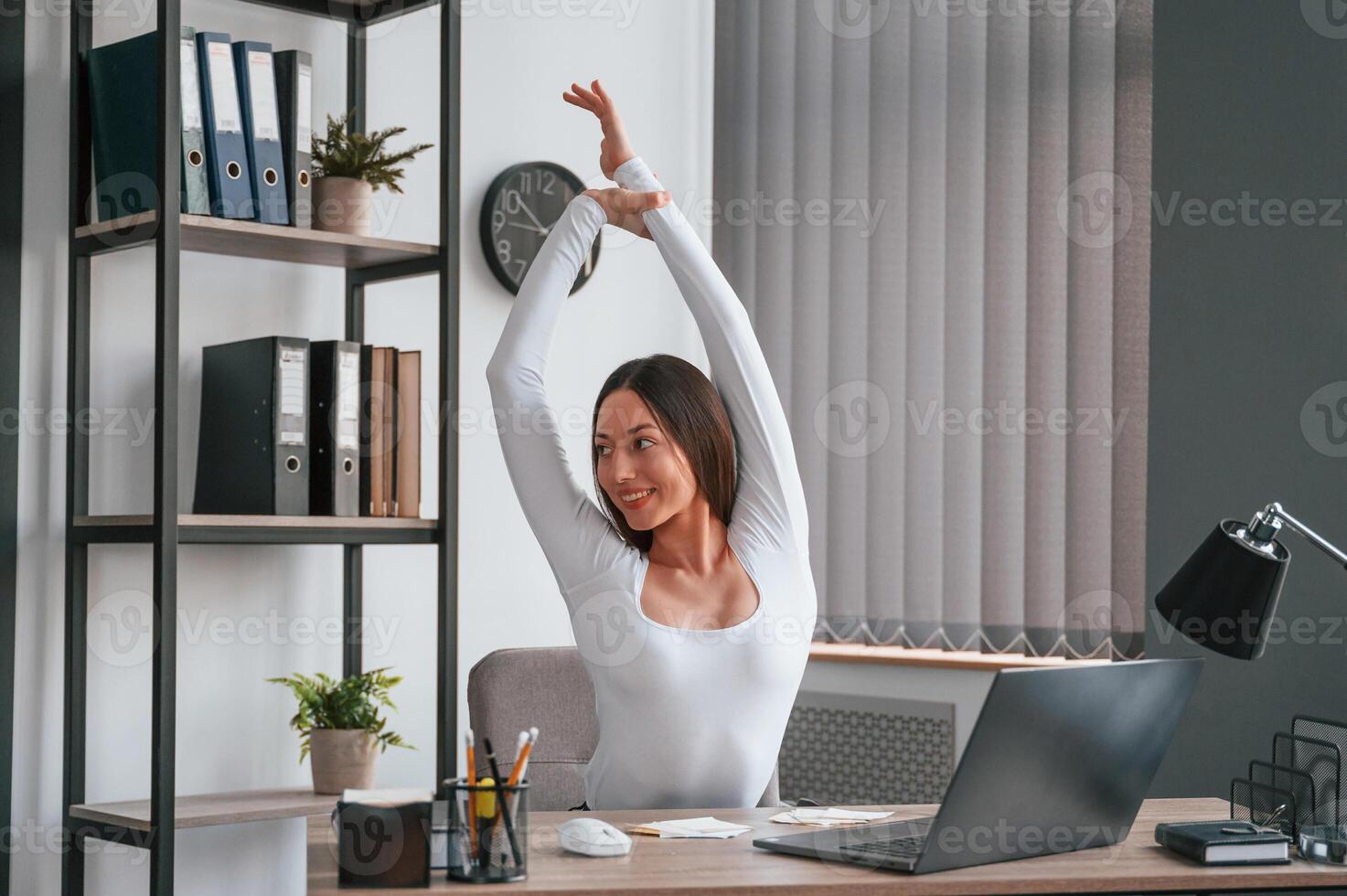 Takes ,a break, stretches her hands. Young beautiful woman in white clothes is in the office photo